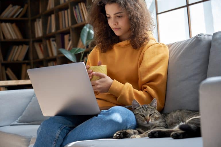 Young girl relaxing on sofa with cat watching series on laptop at home.